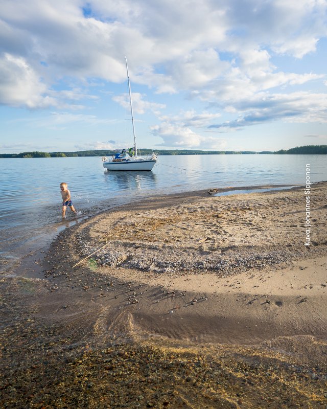 Hiekkatörmä Päijänteen rannalla, vene ja lapsi vanhempansa kanssa