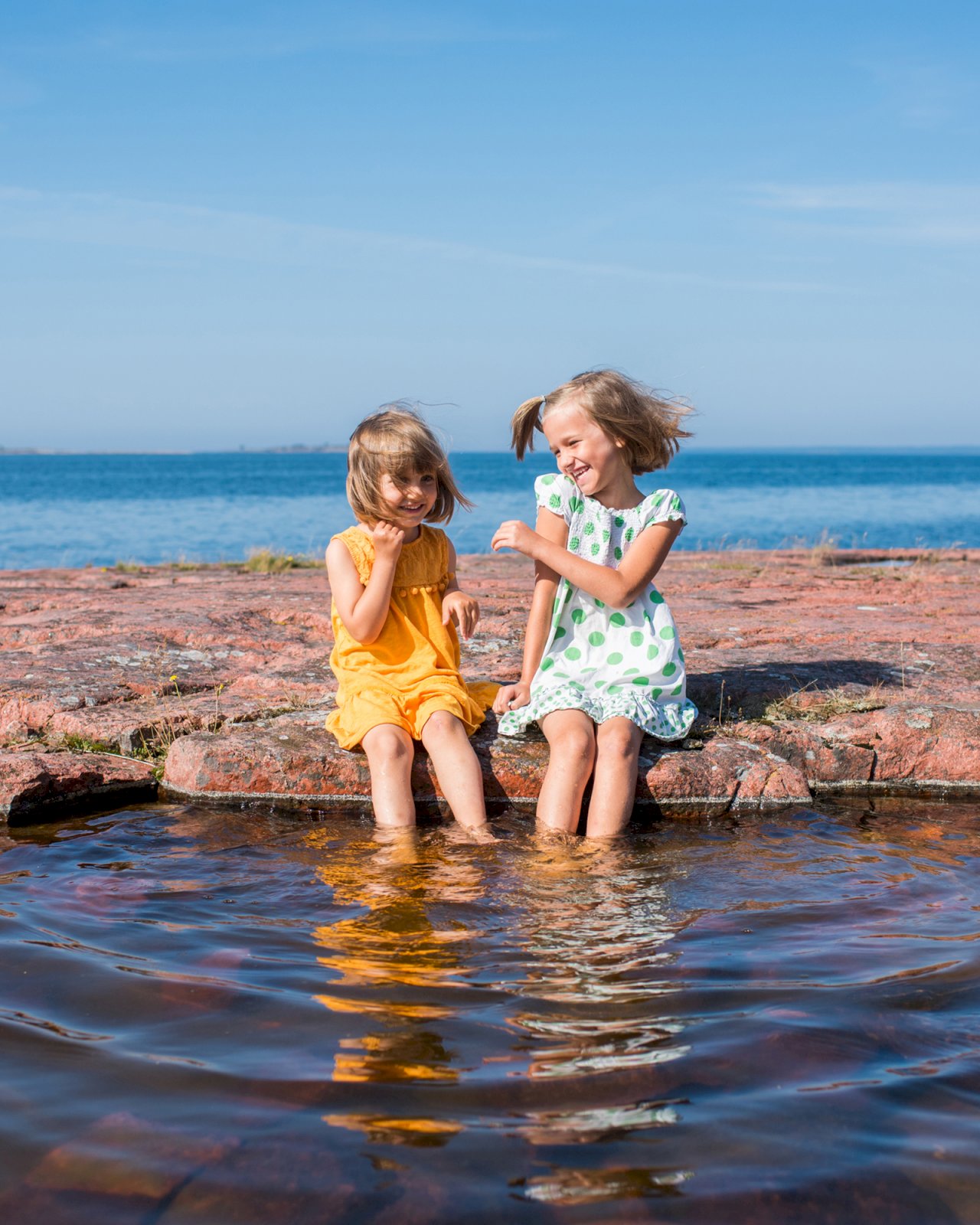 Lapset istumassa Ahvenanmaan kalliolla huljuttamassa jalkoja merivedessä