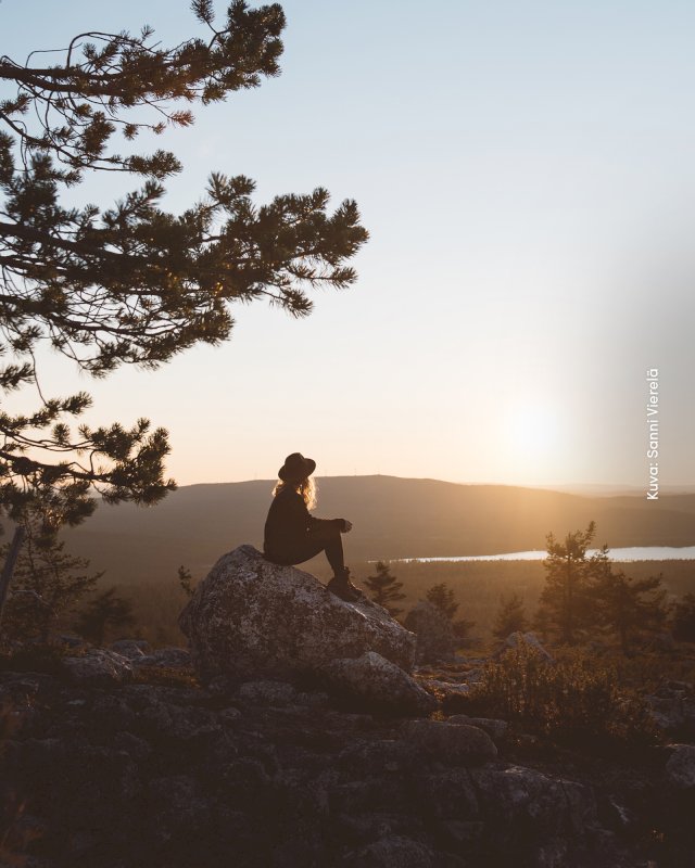 Retkeilijä istuu kalliolla katsellen auringonlaskua Särkitunturilla Muoniossa.
